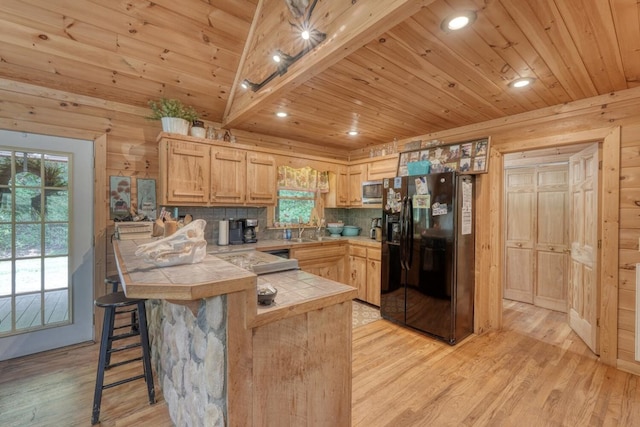 kitchen with light brown cabinetry, tile countertops, black refrigerator with ice dispenser, and light hardwood / wood-style flooring