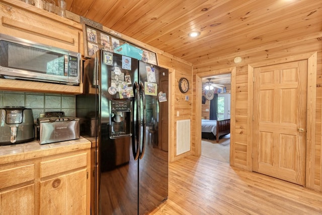 kitchen featuring ceiling fan, wooden ceiling, black fridge, light hardwood / wood-style floors, and wooden walls