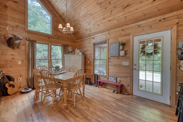 dining area featuring light wood-type flooring, wooden walls, high vaulted ceiling, and a notable chandelier