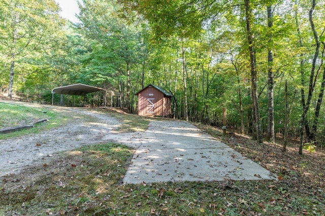 view of yard featuring an outbuilding, a barn, driveway, a carport, and a wooded view