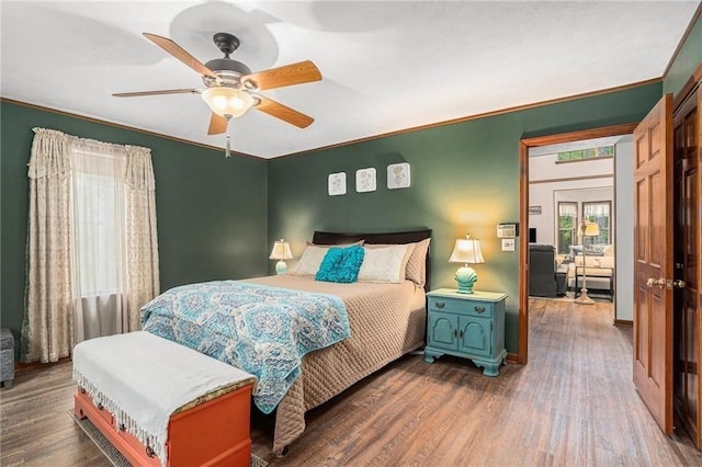 bedroom featuring dark wood finished floors, multiple windows, a ceiling fan, and ornamental molding