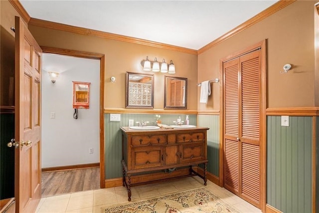 full bathroom featuring tile patterned floors, a wainscoted wall, ornamental molding, a sink, and double vanity