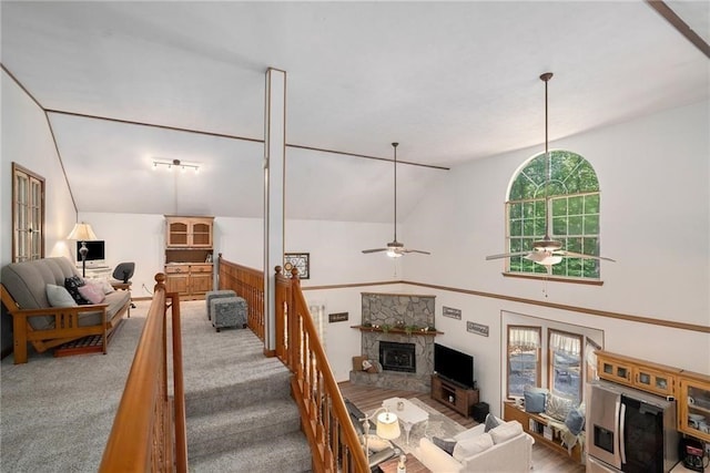 living area featuring carpet floors, high vaulted ceiling, a stone fireplace, and ceiling fan