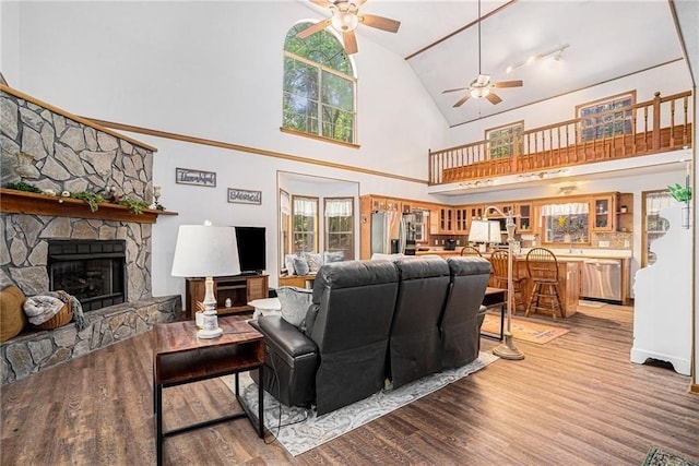 living area with a stone fireplace, light wood-style flooring, high vaulted ceiling, and ceiling fan