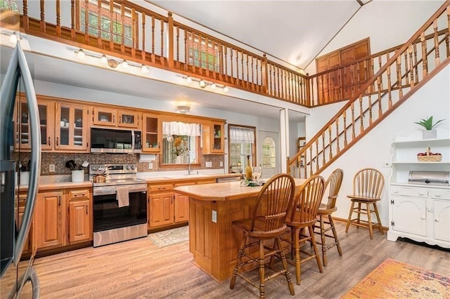 kitchen with light wood-style flooring, a center island, appliances with stainless steel finishes, light countertops, and glass insert cabinets