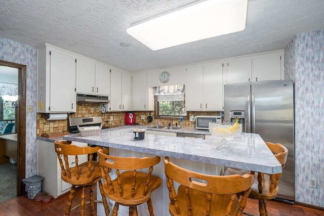 kitchen with white cabinetry, a breakfast bar area, stainless steel appliances, and dark hardwood / wood-style flooring