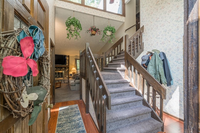 stairway featuring a stone fireplace, hardwood / wood-style flooring, a high ceiling, and a textured ceiling