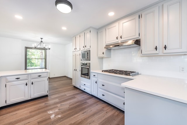 kitchen with appliances with stainless steel finishes, pendant lighting, hardwood / wood-style flooring, an inviting chandelier, and white cabinets