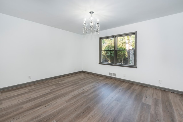 unfurnished room with a chandelier and dark wood-type flooring