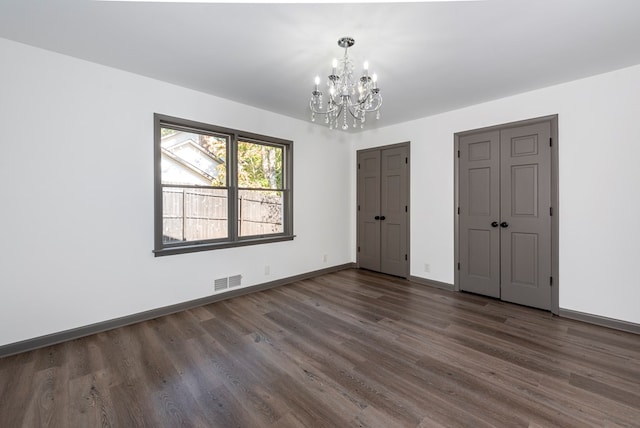 unfurnished bedroom featuring dark hardwood / wood-style flooring, multiple closets, and a notable chandelier