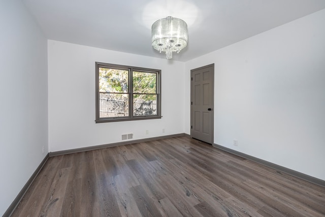 spare room featuring dark hardwood / wood-style flooring and an inviting chandelier