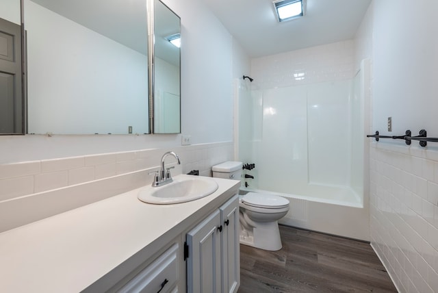 full bathroom featuring tiled shower / bath combo, wood-type flooring, toilet, vanity, and tile walls