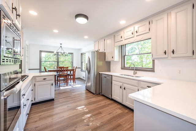 kitchen featuring sink, a wealth of natural light, decorative light fixtures, white cabinetry, and stainless steel appliances