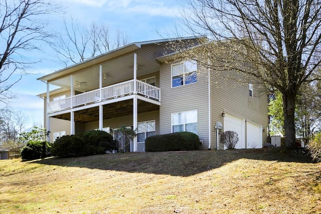 rear view of property with a ceiling fan, a garage, and a lawn