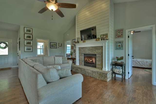 living room with a ceiling fan, high vaulted ceiling, a stone fireplace, and hardwood / wood-style floors