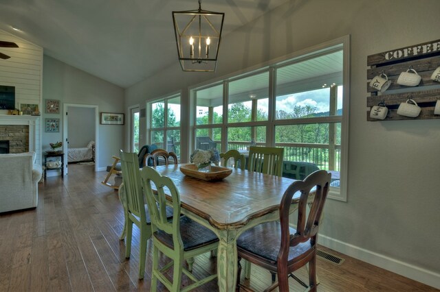 dining room with visible vents, an inviting chandelier, lofted ceiling, a stone fireplace, and dark wood-type flooring