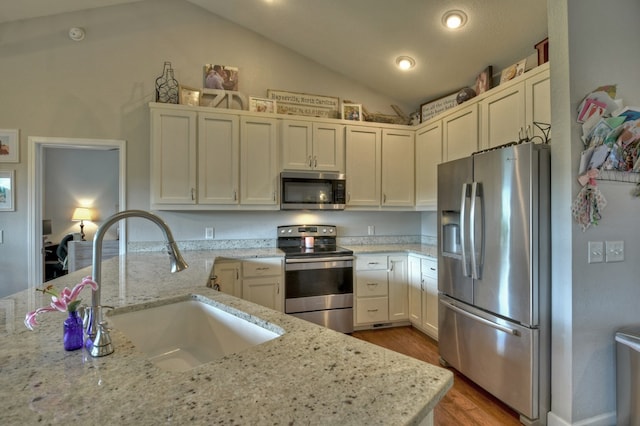 kitchen featuring appliances with stainless steel finishes, wood finished floors, a sink, light stone counters, and lofted ceiling