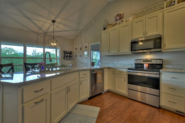 kitchen with wood finished floors, a sink, appliances with stainless steel finishes, a notable chandelier, and vaulted ceiling