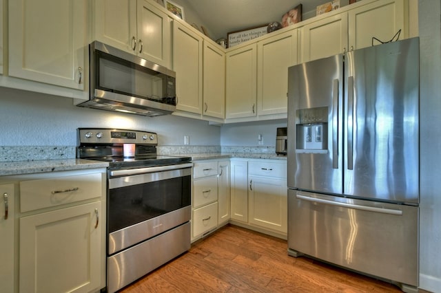 kitchen featuring appliances with stainless steel finishes, light stone counters, and light wood-type flooring