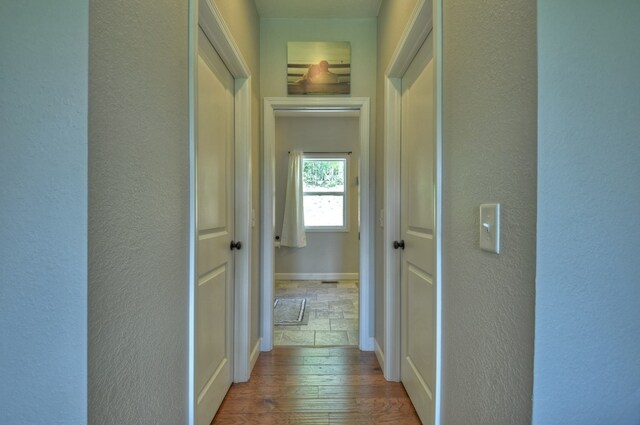 hall featuring baseboards, a textured wall, and hardwood / wood-style floors