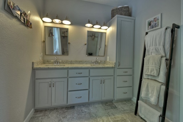 bathroom with double vanity, baseboards, a textured wall, and a sink
