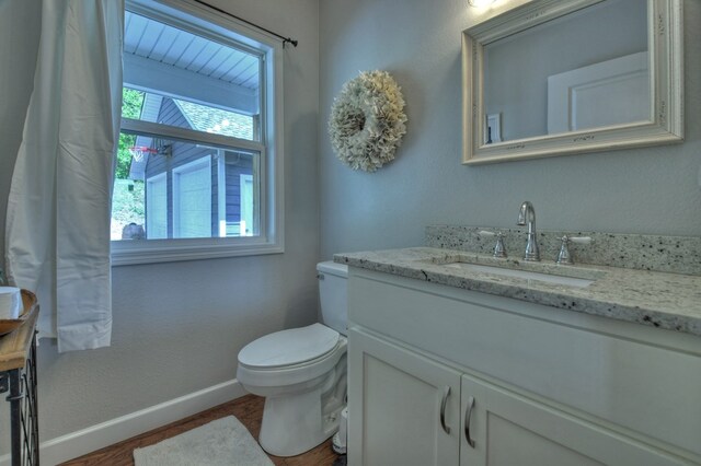 half bath with toilet, baseboards, wood finished floors, and vanity
