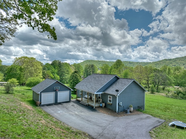 exterior space with a garage, covered porch, roof with shingles, an outbuilding, and a yard