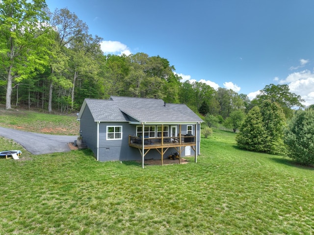 back of house with a shingled roof, a wooden deck, and a yard