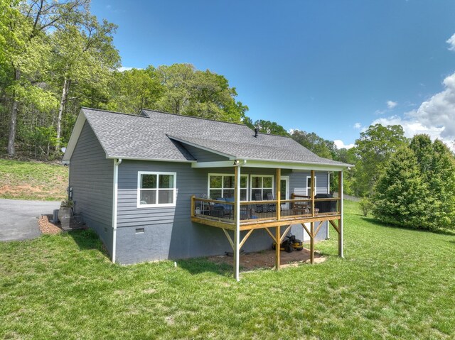 back of property featuring a lawn, roof with shingles, and a deck