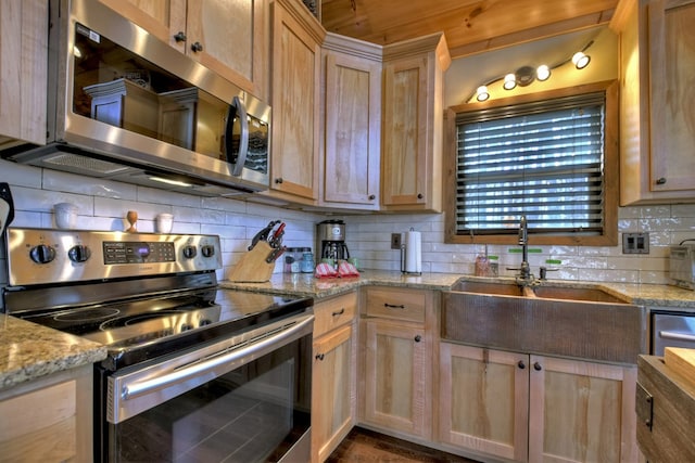 kitchen with a sink, appliances with stainless steel finishes, light stone countertops, light brown cabinetry, and tasteful backsplash