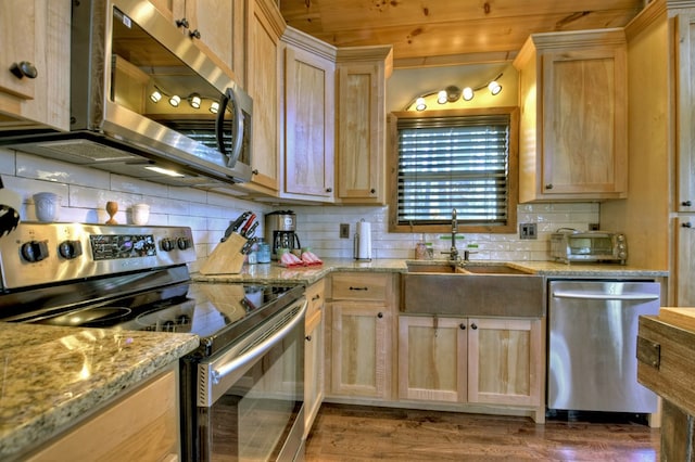 kitchen featuring light stone counters, light brown cabinets, a sink, appliances with stainless steel finishes, and tasteful backsplash