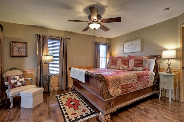 bedroom featuring ceiling fan, multiple windows, wood finished floors, and a wainscoted wall