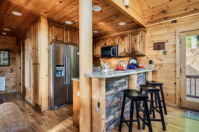 kitchen featuring a kitchen bar, wooden walls, kitchen peninsula, and appliances with stainless steel finishes