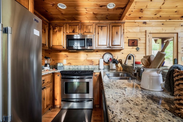 kitchen with sink, wood ceiling, appliances with stainless steel finishes, light stone countertops, and wood walls