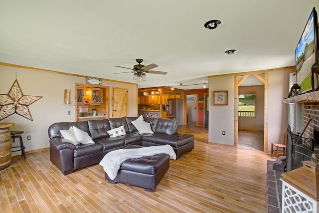 living area featuring ceiling fan, a brick fireplace, and light wood finished floors