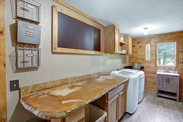 laundry area with independent washer and dryer, cabinet space, a textured wall, wood walls, and light wood-style flooring