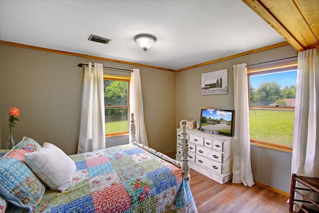 bedroom with crown molding, visible vents, wood finished floors, baseboards, and a textured ceiling