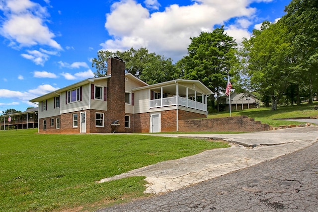 rear view of property featuring a chimney, a yard, and brick siding