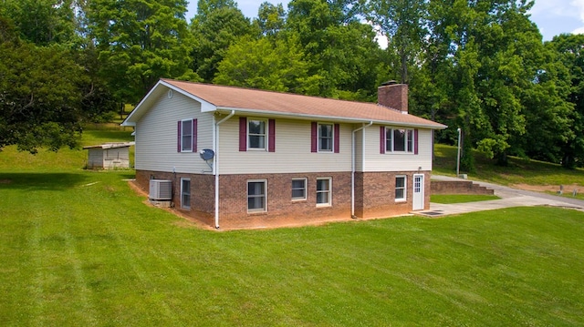 view of property exterior with a lawn, central AC unit, brick siding, and a chimney