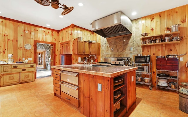 kitchen featuring wood walls, a center island with sink, wall chimney exhaust hood, and sink