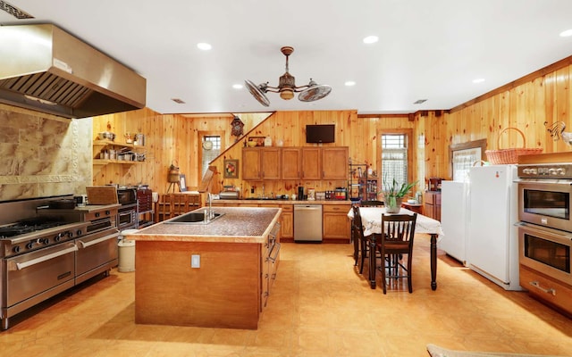 kitchen featuring exhaust hood, stainless steel appliances, ceiling fan, a breakfast bar area, and a kitchen island with sink