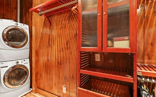 laundry area with wood walls and stacked washer and dryer