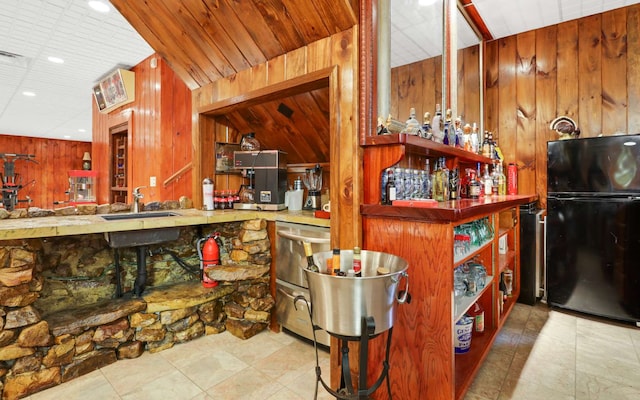 interior space with light tile flooring, lofted ceiling, fridge, wood walls, and sink