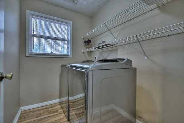 laundry area with separate washer and dryer, a textured ceiling, and light wood-type flooring