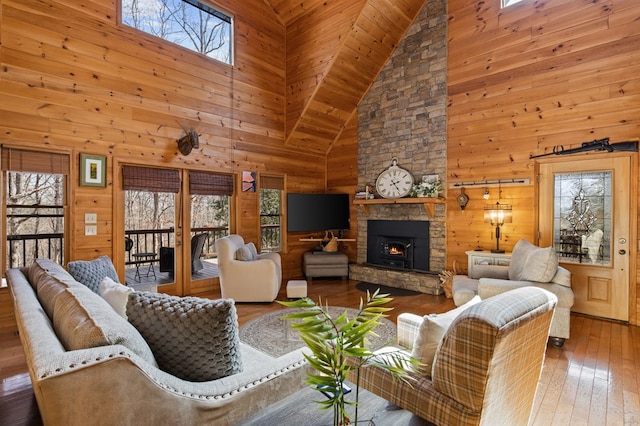 living area with wooden walls, a stone fireplace, lofted ceiling, and hardwood / wood-style flooring