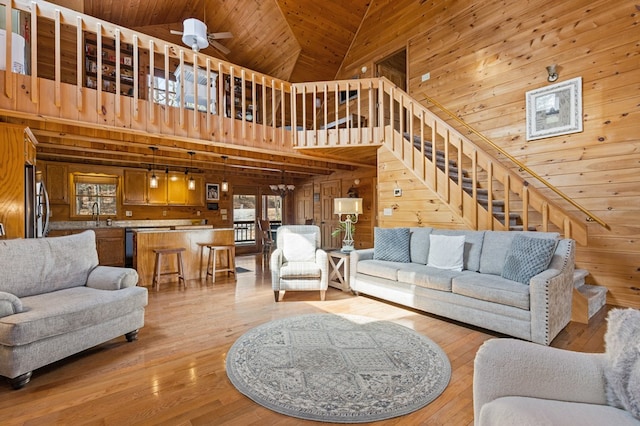 living area featuring stairway, high vaulted ceiling, light wood-style floors, wood walls, and wooden ceiling