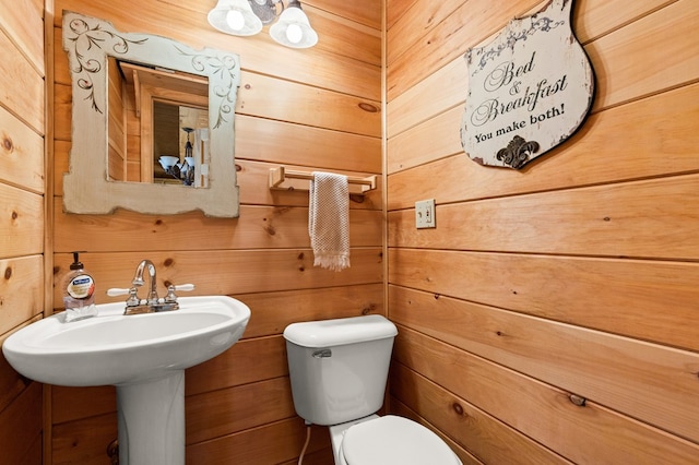 bathroom with a sink, wooden walls, and toilet