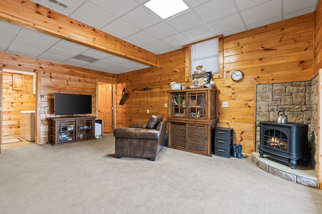 carpeted living room with a wood stove, wooden walls, a paneled ceiling, and visible vents