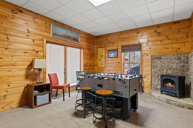 recreation room featuring a paneled ceiling, carpet, wood walls, and a wood stove