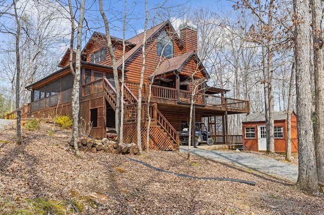 view of front of home with log veneer siding, a sunroom, a chimney, stairs, and a deck